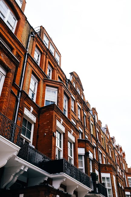 Photograph of a multi-story residential building with a classic Victorian architectural style, featuring a brown brick facade complemented by white decorative window frames, cornices, and moldings. Th